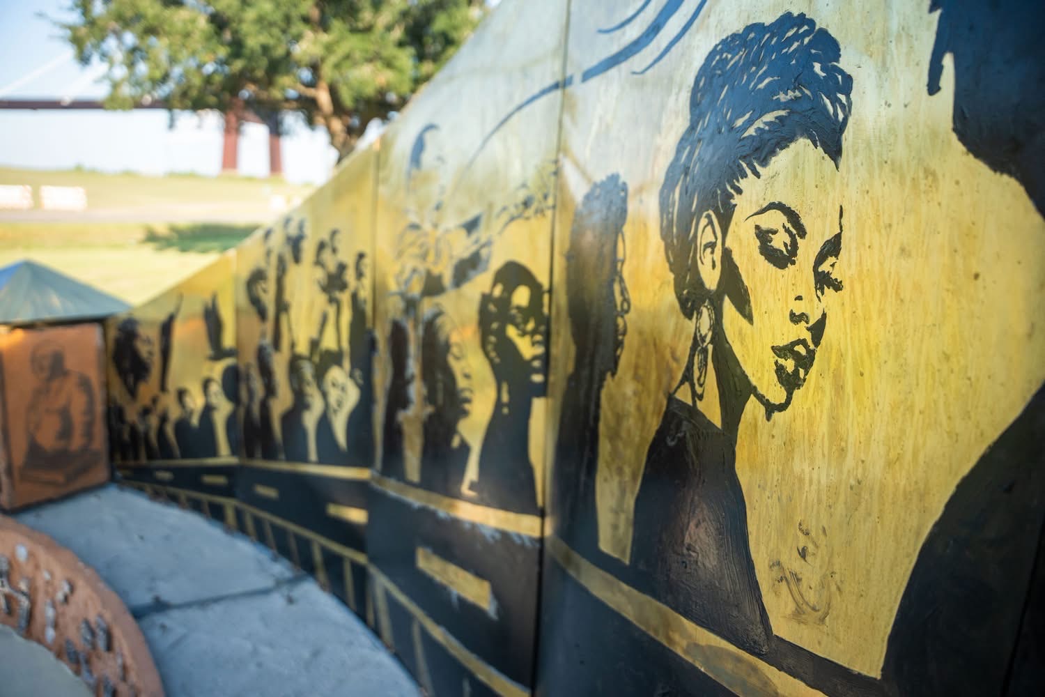 Curved memorial wall of hand-painted trailblazer portraits in black and gold