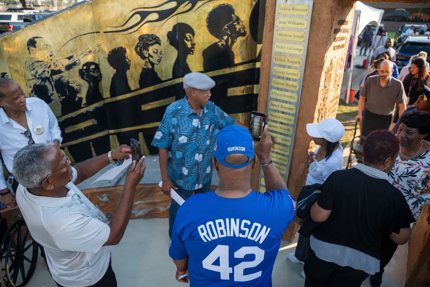 Dedication guests photographing the mural as a name plaque column is read