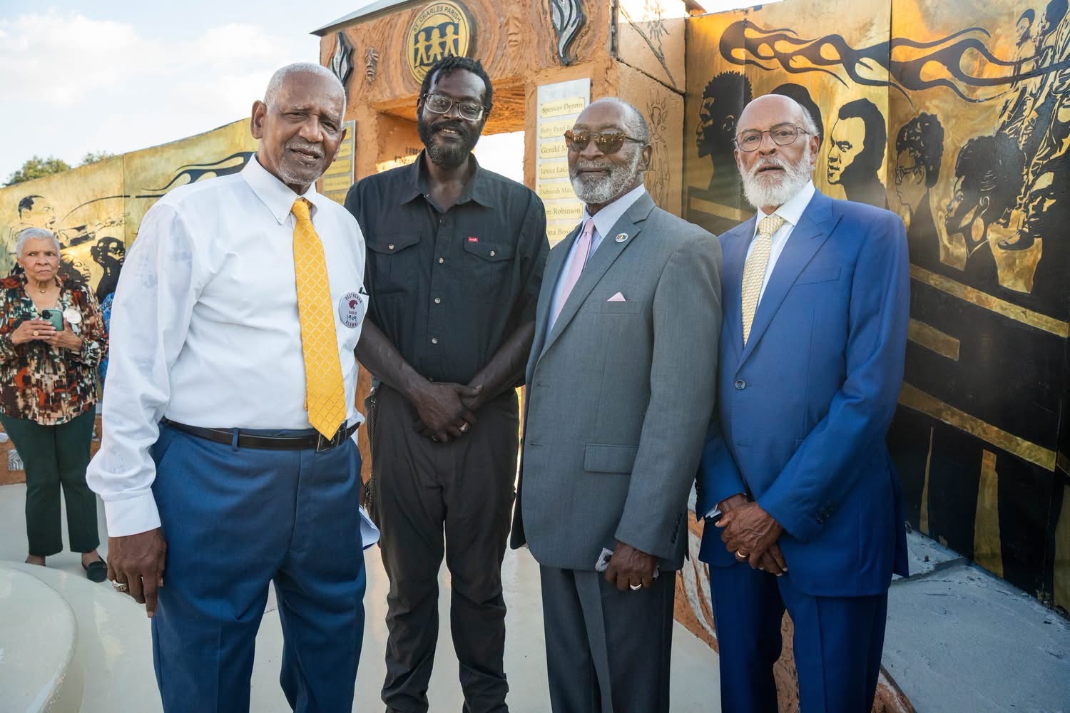 Three trailblazers standing together with Derrick Monk in front of the mural